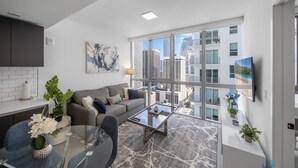 A modern living room with a glass coffee table, grey sofa, and a view of the city through large windows. - Apartment at Downtown Miami (Miami)