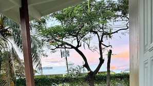 Una terraza de madera con una sola silla Adirondack, piso de baldosas y vista a un árbol y edificios a lo lejos.