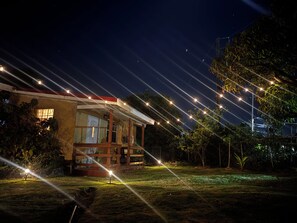 A house with a porch, a lawn, and string lights. - Orchard House Bachelor w/ kitchenette (Gros-islet)