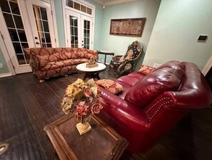 A living room with a red leather armchair, a patterned sofa, and a small round table with a vase of flowers. - Serenity Retreat at Shenandoah (Dubach)