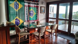 A dining area with a glass table, four chairs, and Brazilian flags. - Alugo Casa Para Temporada em Búzios-rj (Lot. Portal da Ferradura Arm. dos Búzios)