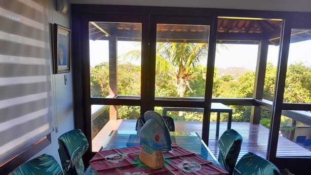 A dining area with a glass table, four chairs, and a decorative centerpiece. - Alugo Casa Para Temporada em Búzios-rj (Lot. Portal da Ferradura Arm. dos Búzios)