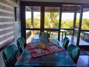 A dining area with a glass table, four chairs, and a decorative centerpiece. - Alugo Casa Para Temporada em Búzios-rj (Lot. Portal da Ferradura Arm. dos Búzios)
