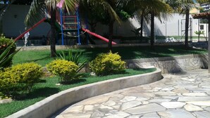 A stone pathway leading to a playground with a red slide and a blue climbing structure. - Alugo Casa Para Temporada em Búzios-rj (Lot. Portal da Ferradura Arm. dos Búzios)