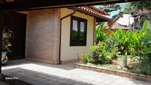 A brick building with a tiled patio and a garden with various plants and flowers. - Alugo Casa Para Temporada em Búzios-rj (Lot. Portal da Ferradura Arm. dos Búzios)