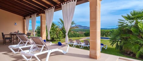 A covered outdoor area with lounge chairs, a table, and a view of the landscape.
