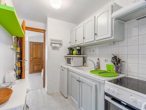 Een kleine keuken met witte kastjes, een magnetron, een fornuis en een spoelbak.