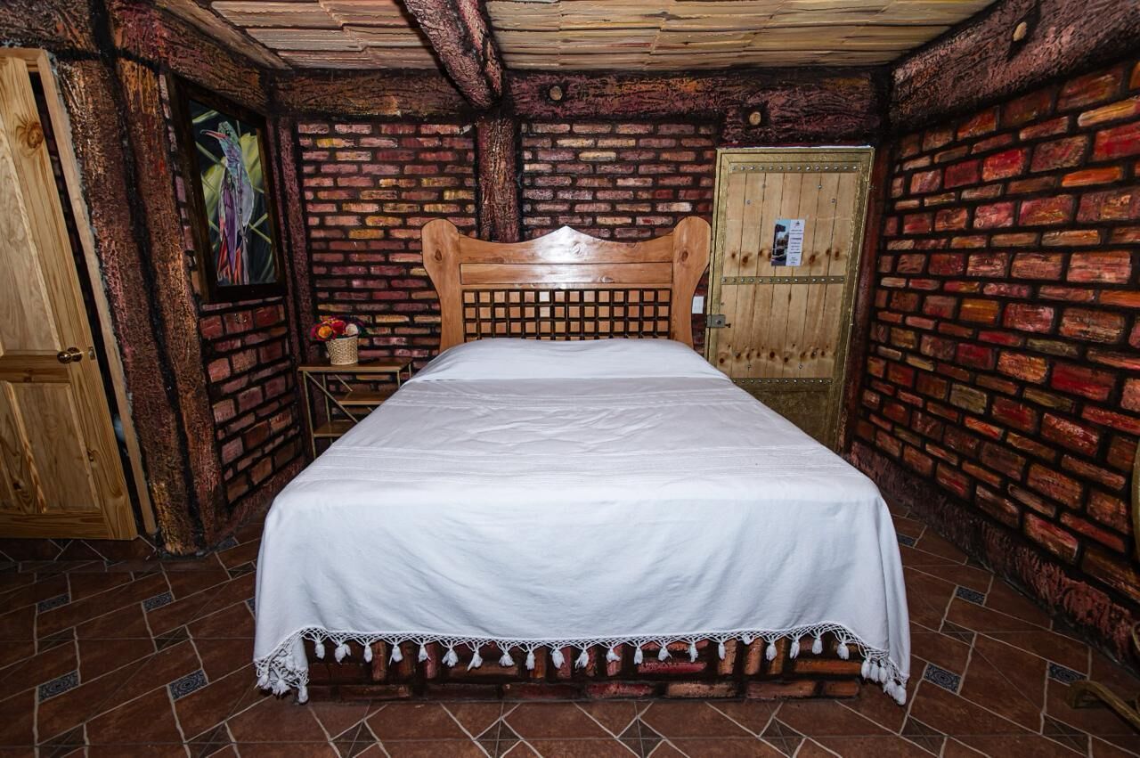 Quarto com cama de madeira, paredes de tijolo e chão ladrilhado.