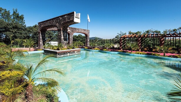 Une piscine aux eaux cristallines, agrémentée d’une arche en pierre et d’une pergola, au cœur d’un jardin aménagé.