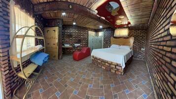 Una habitación con pared de ladrillo, una cama, una silla roja, un estante de madera y una puerta.
