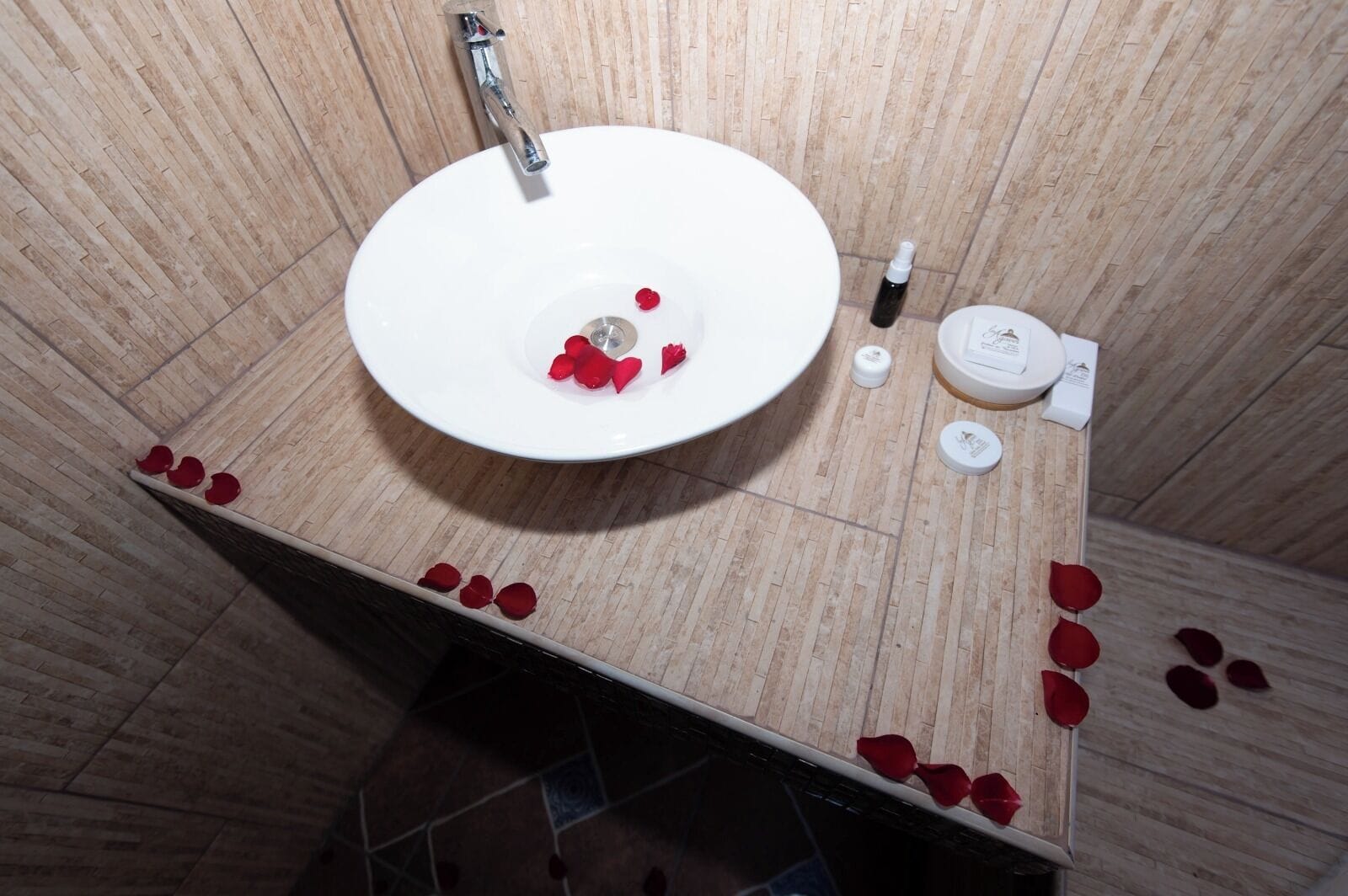 A bathroom with a white sink, a handheld showerhead, and rose petals scattered on the floor.