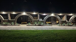 Une rangée de bâtiments en briques, dotés d’entrées en arc de cercle et éclairés par des lampes suspendues, avec une pelouse bien entretenue au premier plan.