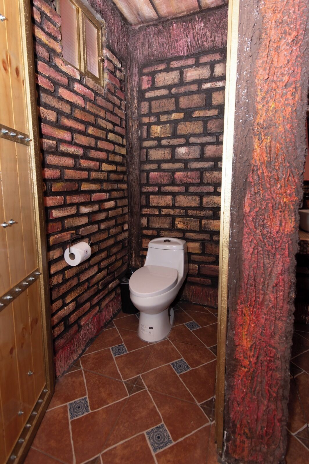 A small, rustic bathroom with a brick wall, a toilet, and a wooden door.