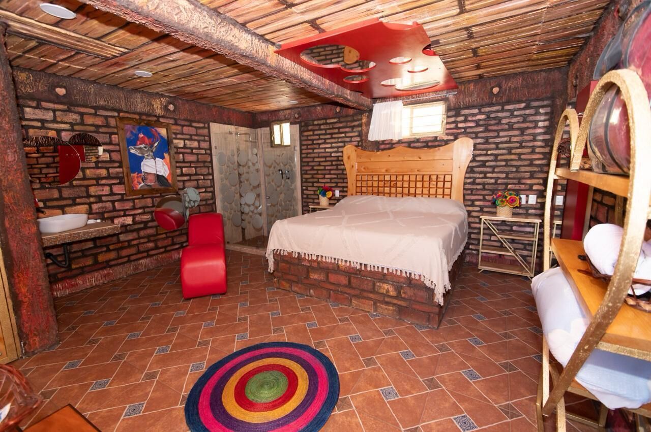 Una habitación rústica con una cama de madera, una silla roja, una mesita pequeña y una alfombra colorida.