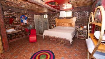 Una habitación rústica con una cama de madera, una silla roja, una mesita pequeña y una alfombra colorida.