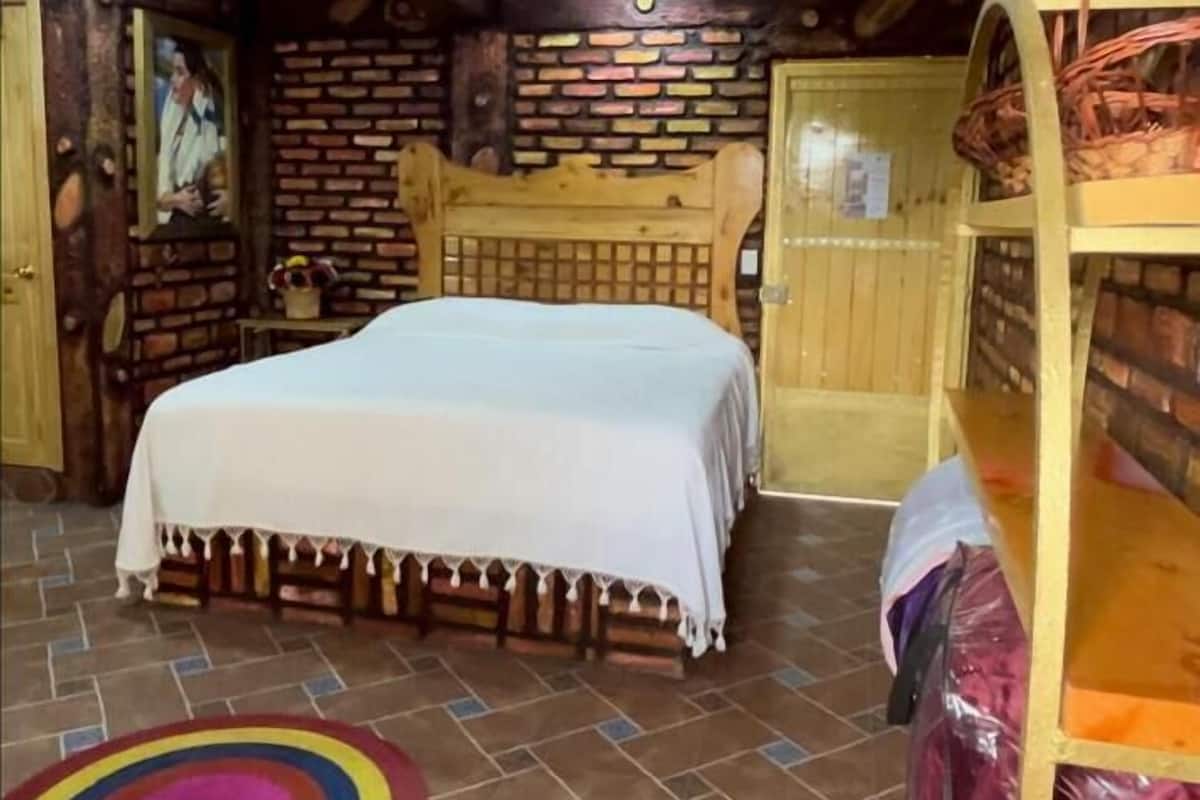 A rustic room with a wooden ceiling, a bed, a bench, and a brick wall.