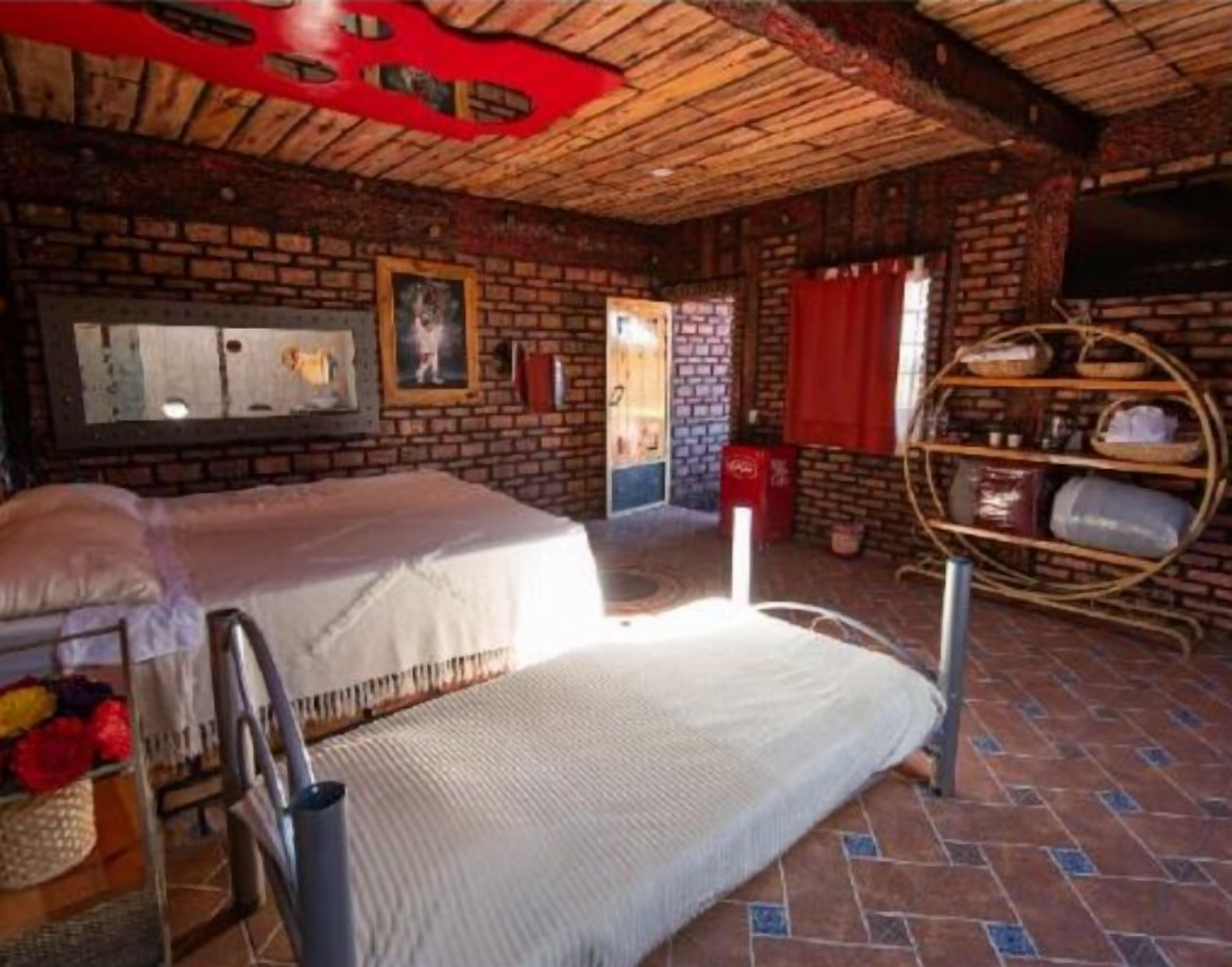 Una habitación rústica con pared de ladrillo, techo de madera y cama con colchón blanco.