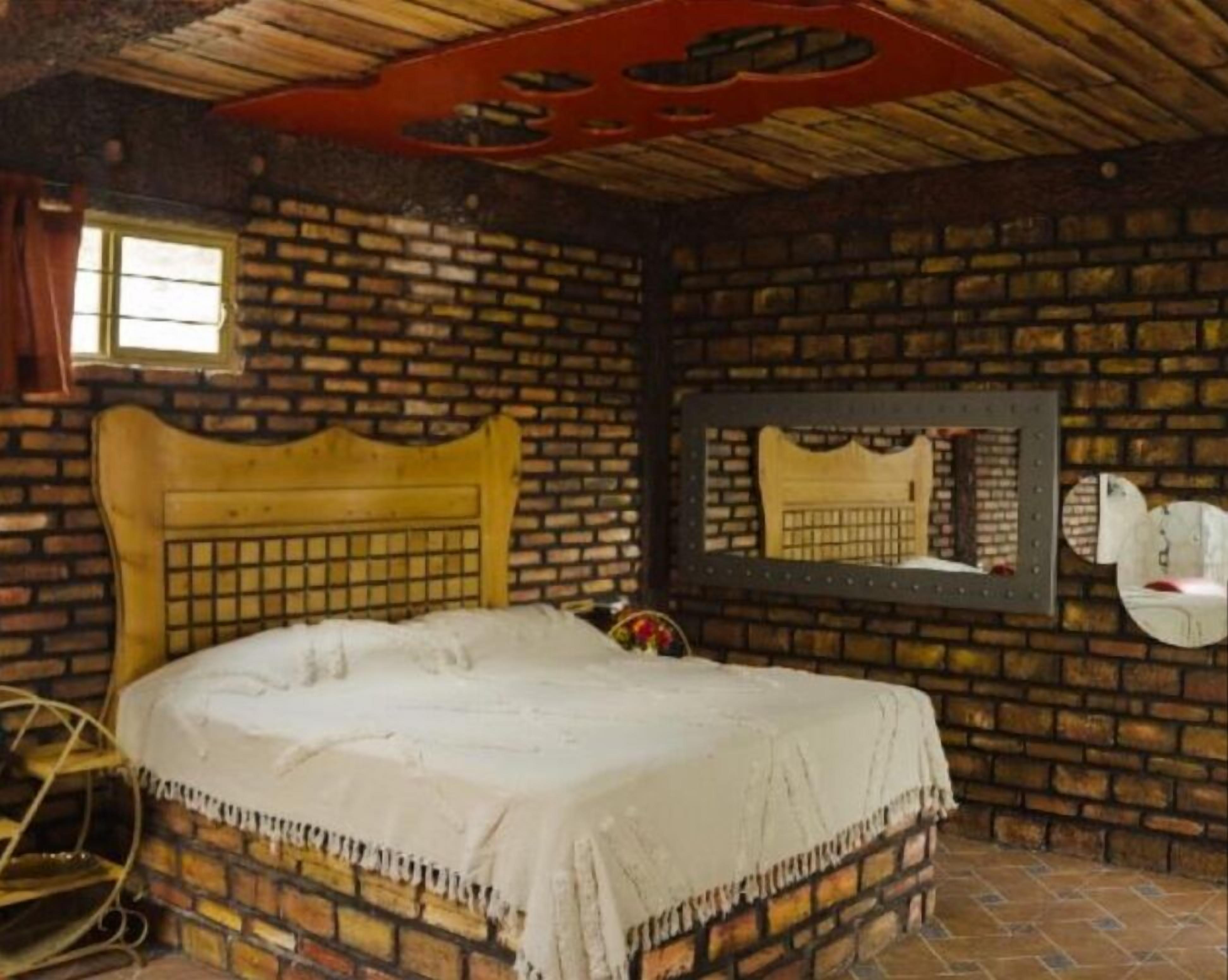 A rustic room with a brick wall, a wooden bed, a mirror, and a window.