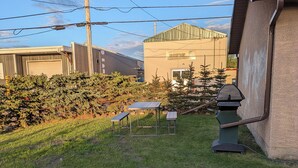 A grassy yard with solar panels, a barbecue grill, and a building with a sign reading "BISON". - Small House in Downtown Wainwright (Wainwright)
