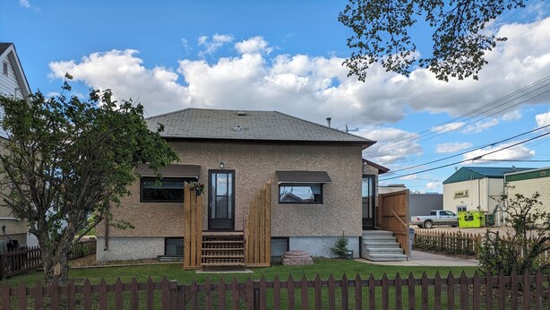 A two-story house with a stone facade, a front porch, and a wooden fence. - Small House in Downtown Wainwright (Wainwright)