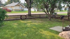 A residential backyard with a wooden fence, a lawn, and a house in the background. - Small House in Downtown Wainwright (Wainwright)