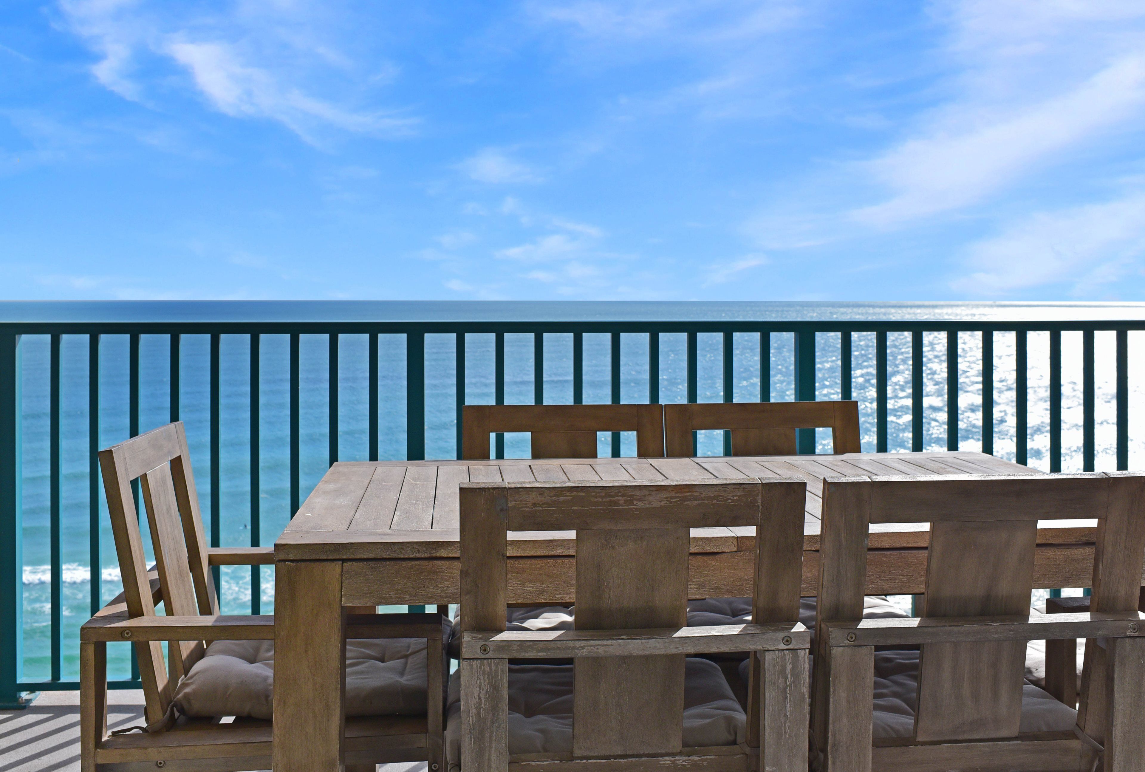 A wooden table and chairs on a balcony with a view of the ocean.