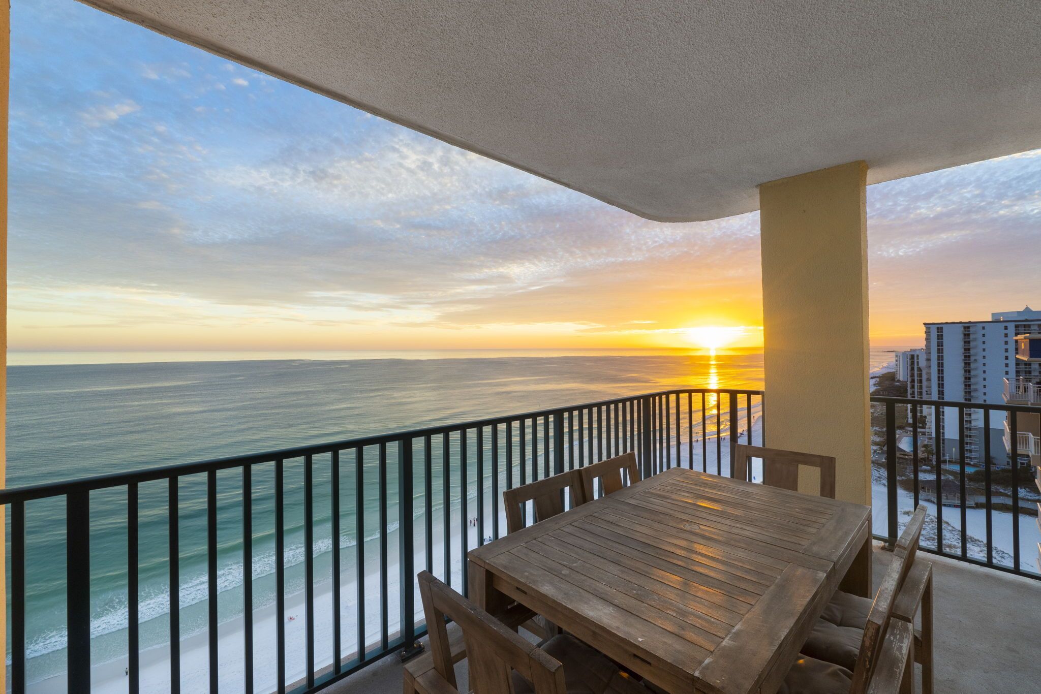 Un balcon avec une table et des chaises en bois, d’où l’on peut admirer le coucher de soleil sur l’océan.