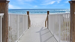 Une promenade en bois qui mène à une plage de sable et offre une vue sur l’océan.