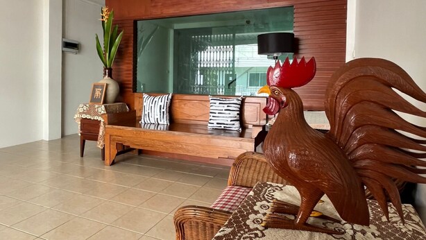 A modern interior with a wooden wall, a large mirror, a wooden bench, and a decorative rooster statue. - Experience the Essence of Friendship: in the Heart of the Old Town (Phuket)
