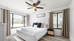 A bedroom with a large bed, a ceiling fan, a nightstand, and a window with curtains. - Relaxing Three Bedroom in PGA National (Palm Beach Gardens)