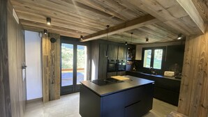 Una cocina moderna con una isla grande, muebles oscuros y vigas de madera en el techo.