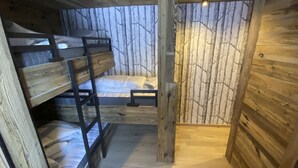 Interior de una cabaña con literas, una cama individual y techo de madera.