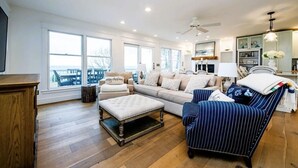 A spacious living room with a large window, a sofa, a striped armchair, and a wooden coffee table.