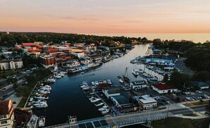 En vy från ovan över en småbåtshamn med förtöjda båtar, en väg som löper längs med hamnen och byggnader i bakgrunden.
