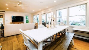 A spacious living room with a large white dining table, a ceiling fan, and a television.