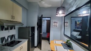 Cozinha compacta com geladeira, fogão e armários. Possui uma área de jantar com mesa e cadeiras, e uma pequena planta em vaso.