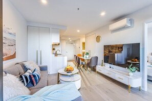 A modern living room with a sofa, coffee table, TV, and dining area.