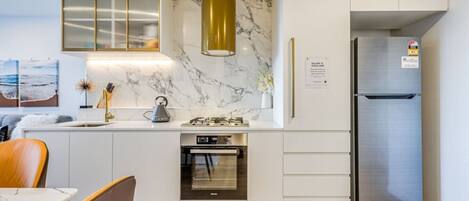 Uma cozinha moderna com forno embutido, geladeira de aço inoxidável e painel de parede de mármore.