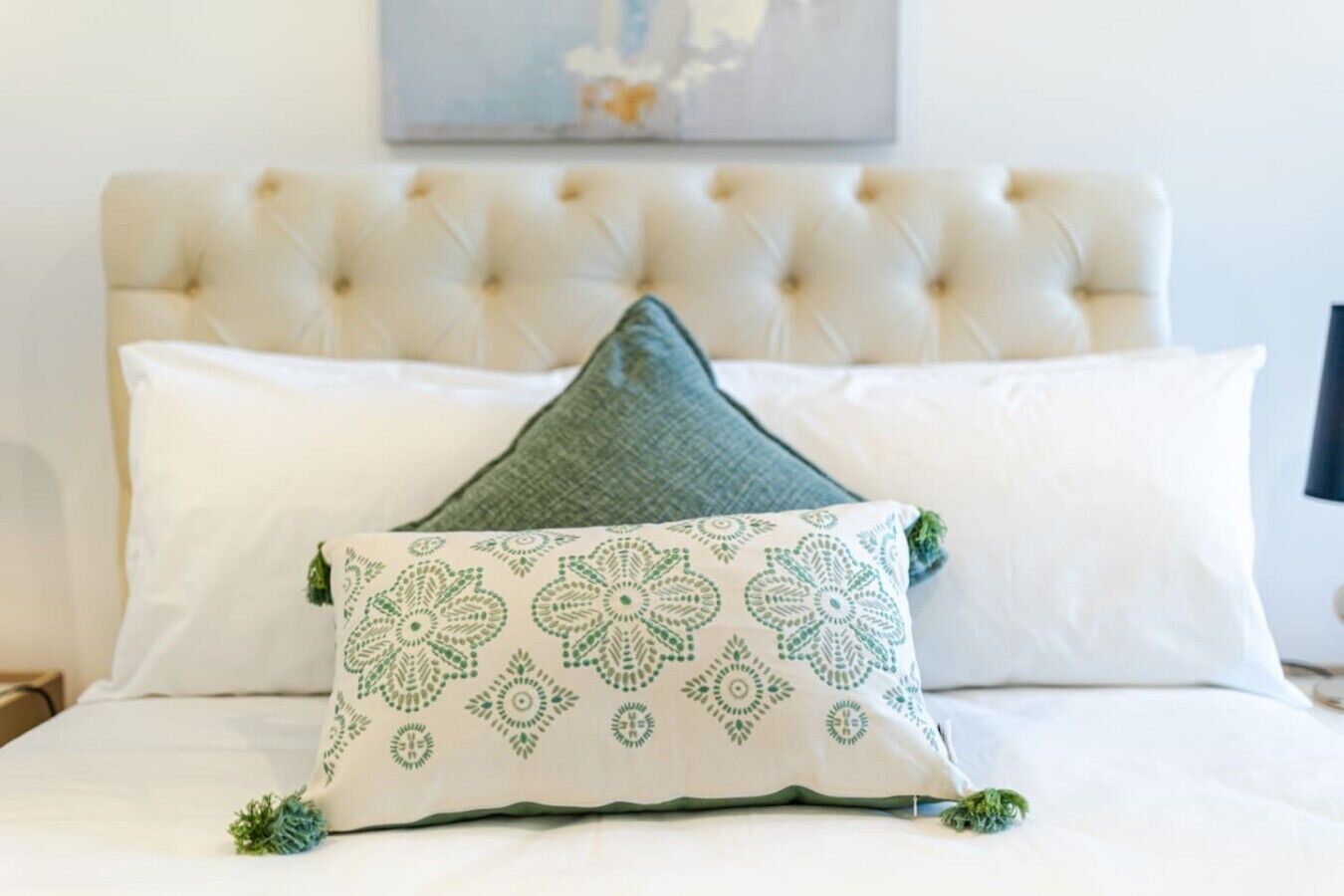 A bed with a tufted headboard, two pillows, and a decorative pillow with a floral pattern.