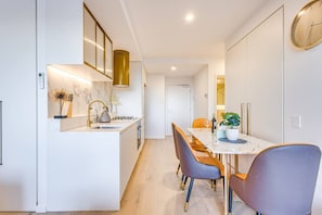 A modern kitchen with a marble countertop, a built-in oven, and a dining area with a table and chairs.