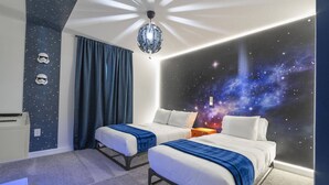 A room with two beds, a starry wall mural, and a ceiling light fixture.