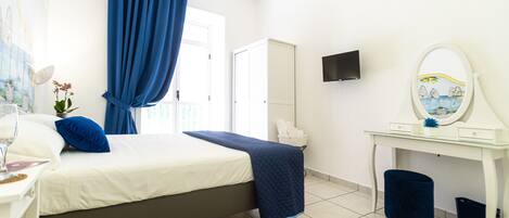 A bedroom with a bed, a desk, a chair, a television, and a window with curtains.