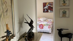 A hallway leading to a bedroom with a bed, a dresser with a sculpture, and a wall clock.