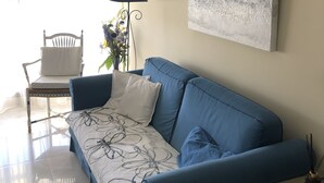 A living room with a blue sofa, a white chair, a floor lamp, and a painting on the wall.