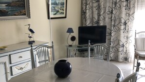 A dining area with a round table, chairs, a vase, a lamp, a television, and artwork on the walls.