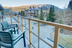 Enjoy breathtaking views of the surrounding mountains from this balcony, featuring comfortable seating and a traditional building in the distance.