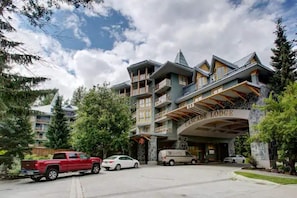 Experience the grand entrance of The Cascade Lodge, featuring a prominent facade and large overhang, with multiple balconies and a distinctive peaked roof.