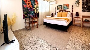 Un dormitorio con una cama, ventilador de techo, televisión y obras de arte en las paredes.