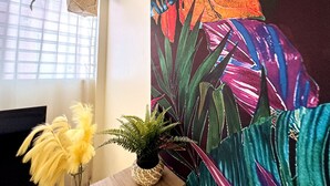 Una habitación con ventana, una pared con un mural tropical y una mesa de madera con una planta en maceta.