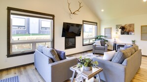 A spacious living room with large windows, a fireplace, and a mounted deer antler. - Pet-Friendly Bozeman Home ~ 7 Mi to Downtown! (Bozeman)